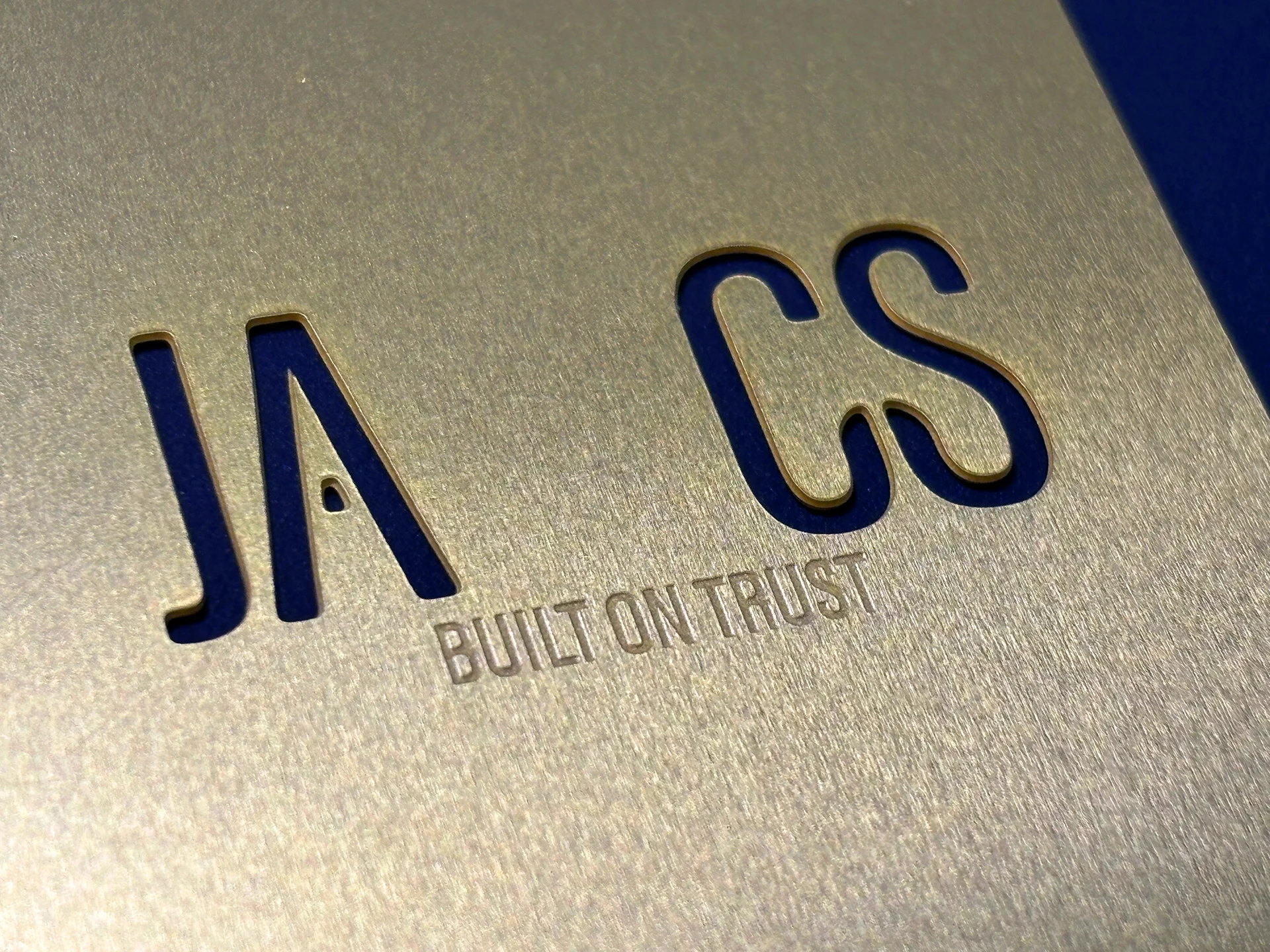 Ja-cs brand logo laser cut gold metal business card with etched "built on trust" writing.